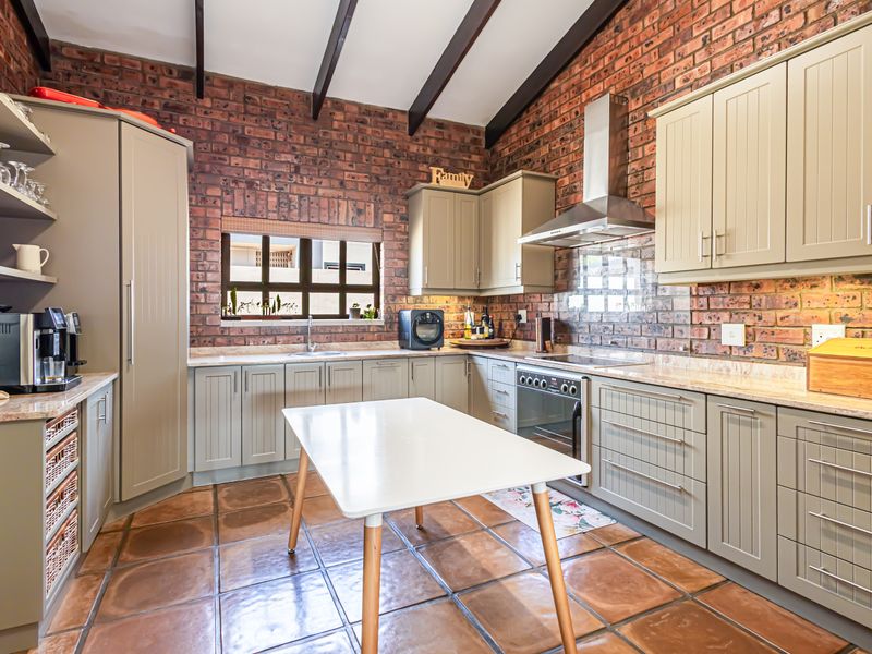 A well-maintained kitchen featuring exposed brick walls, timber ceiling beams, shaker-style cabinetry, stone countertops, and terracotta floor tiles.