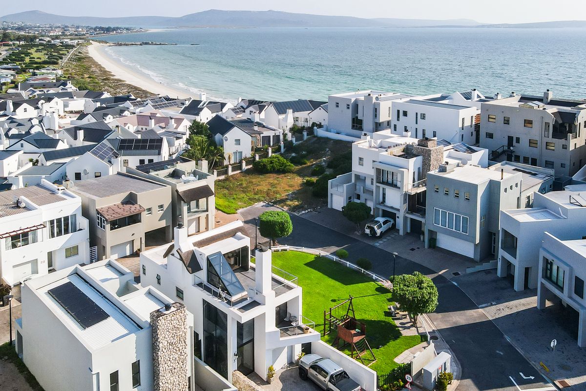 An aerial view of a modern coastal residential estate featuring contemporary homes with solar panels, stone accents, and proximity to the beach.