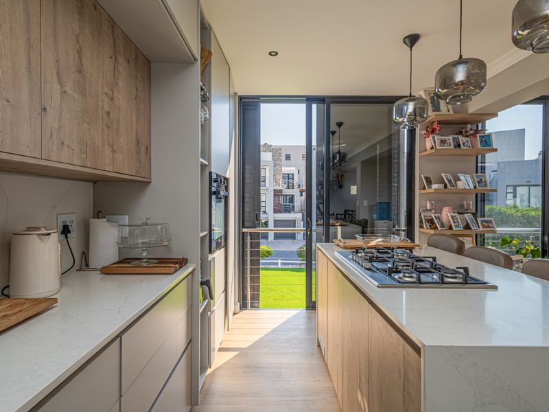 Modern kitchen featuring a central island with a gas hob, stone countertops, wood-look cabinetry, and large sliding glass doors leading to the exterior.