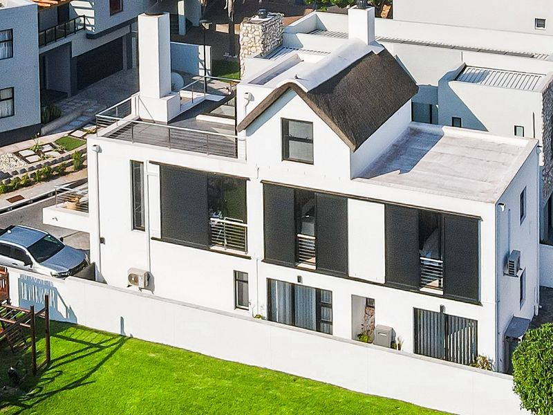 Aerial view of a modern multi-story house featuring a thatched roof section, multiple balconies, and a private garden area with boundary walls.