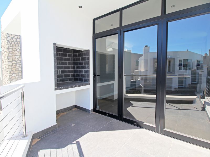 A modern covered balcony featuring tiled flooring, a built-in braai, and large aluminium sliding doors providing seamless indoor-outdoor flow.