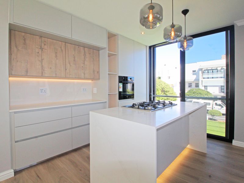 Modern kitchen featuring a central island with a gas hob, sleek cabinetry, stone countertops, and floor-to-ceiling windows providing ample natural light.