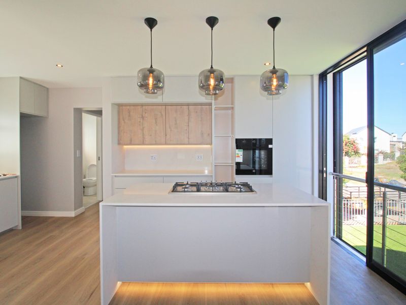 Modern kitchen featuring a central island with a gas cooktop, built-in oven, sleek cabinetry, and large sliding doors leading to an outdoor area.