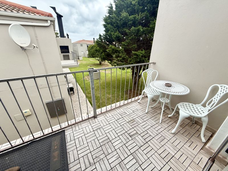 A balcony area featuring metal railings and tiled flooring, overlooking a shared garden space.
