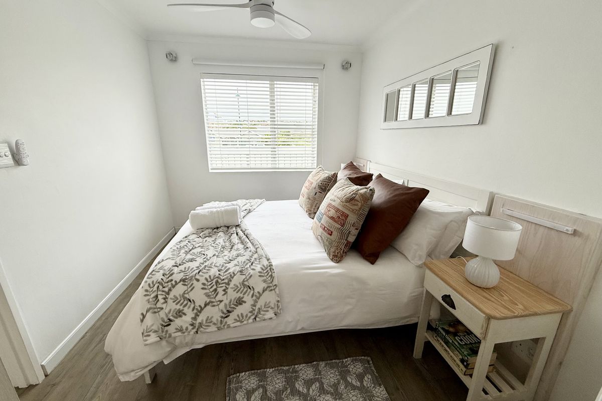 A well-maintained bedroom featuring laminate flooring, a ceiling fan, and a window with venetian blinds, offering a clean and functional living space.