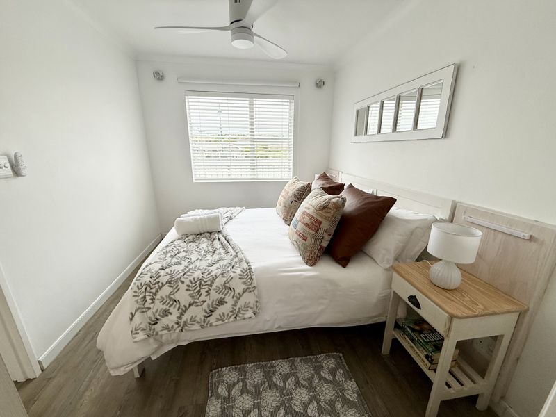 A well-maintained bedroom featuring laminate flooring, a ceiling fan, and a window with venetian blinds, offering a clean and functional living space.