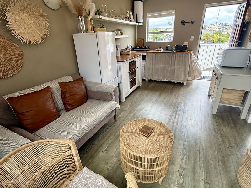 Open-plan living area featuring laminate flooring, a compact kitchenette with sink and cabinetry, and direct access to a balcony.