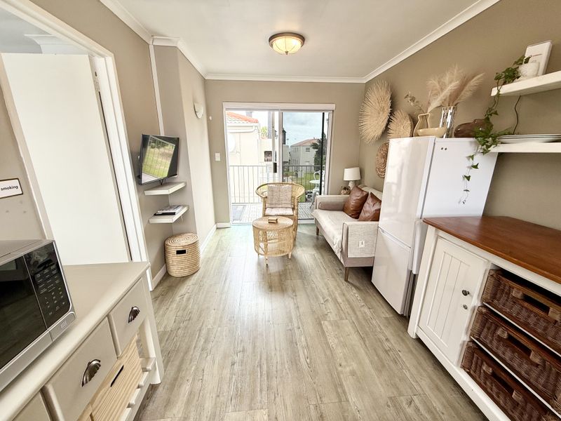 An open-plan living area featuring laminate flooring, neutral wall tones, and a sliding glass door providing direct access to a private balcony.