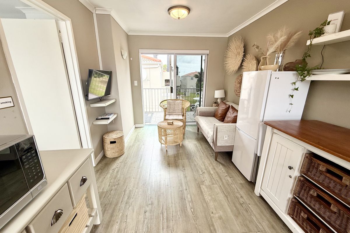 An open-plan living area featuring laminate flooring, neutral wall tones, and a sliding glass door providing direct access to a private balcony.