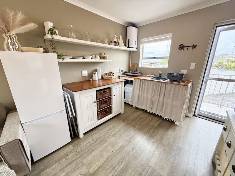 A compact kitchen area featuring laminate flooring, floating shelving, a sink, and direct access to an outdoor balcony through a glass door.