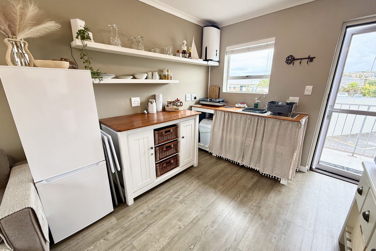 A compact kitchen area featuring laminate flooring, floating shelving, a sink, and direct access to an outdoor balcony through a glass door.