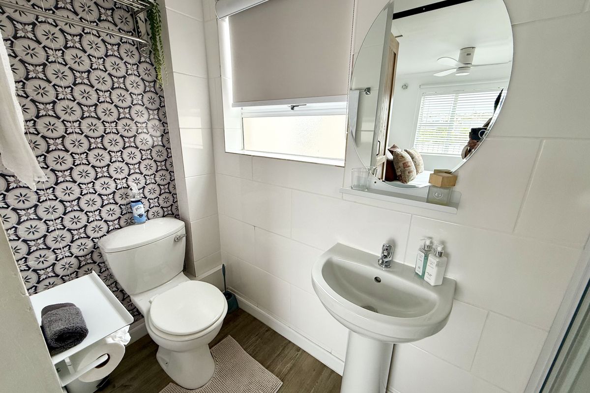 A well-maintained bathroom featuring a pedestal basin, toilet, and a decorative tiled feature wall with modern finishes.