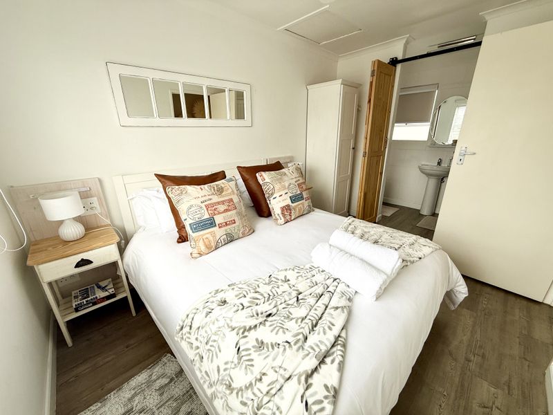 A well-maintained bedroom featuring laminate flooring, a sliding barn door leading to an en-suite bathroom with a pedestal basin, and built-in storage.