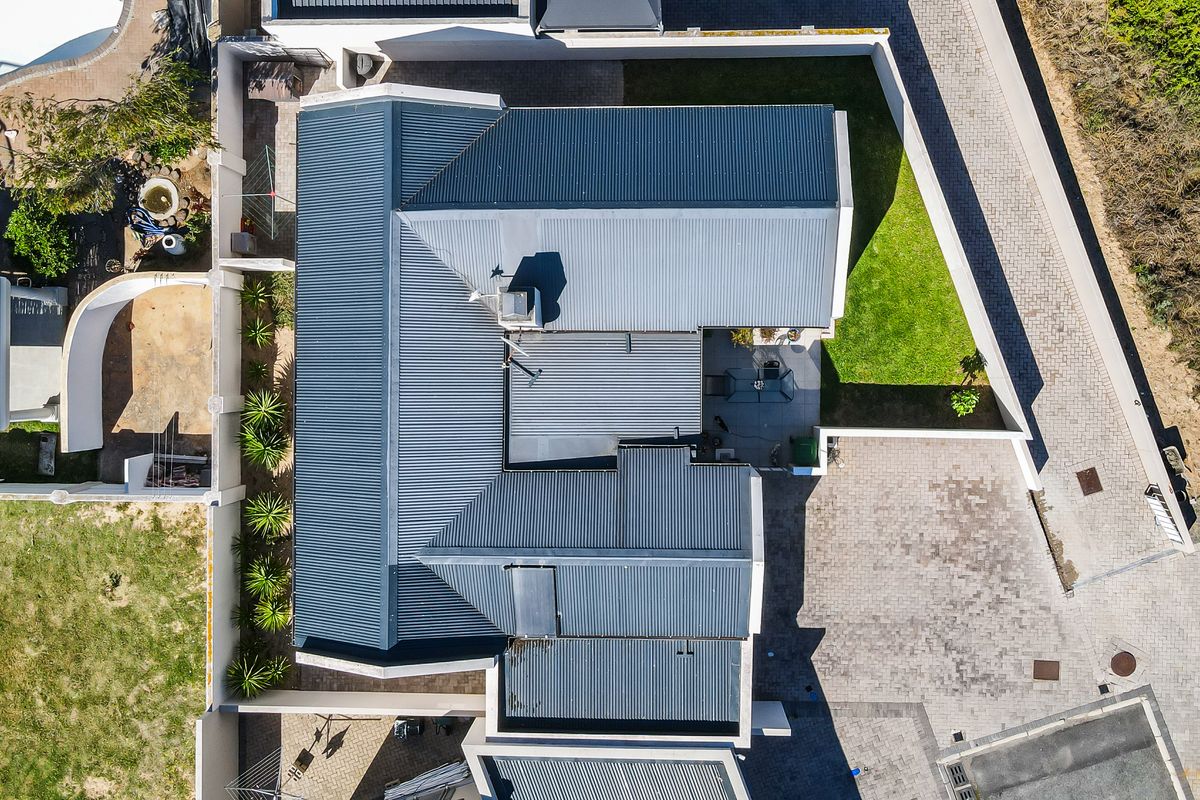 An aerial view of the property showcasing the corrugated metal roof, paved driveway, boundary walls, and landscaped garden area.