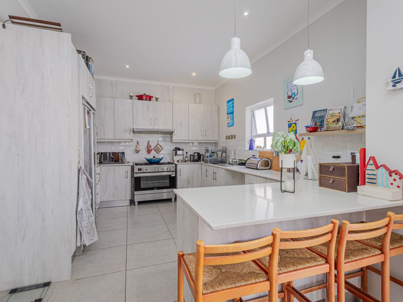 Modern kitchen featuring light wood-grain cabinetry, stone countertops, stainless steel appliances, tiled flooring, and a breakfast bar with pendant lighting.