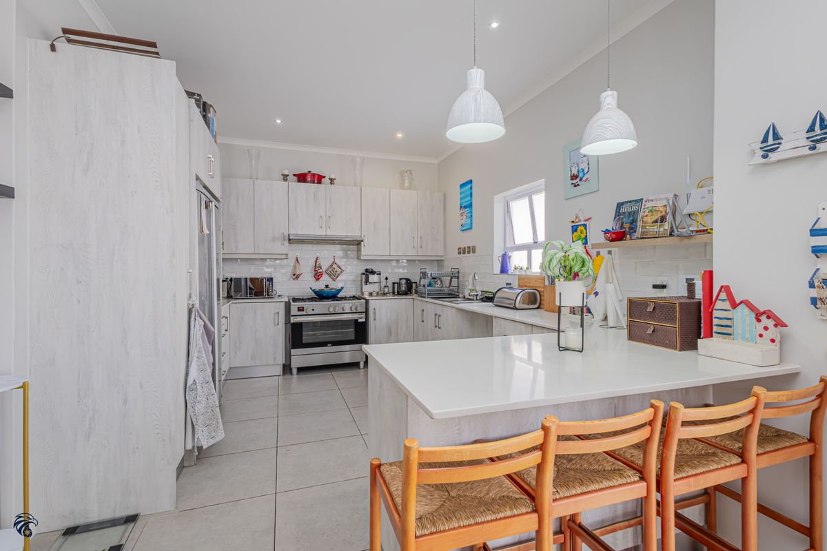 Modern kitchen featuring light wood-grain cabinetry, stone countertops, stainless steel appliances, tiled flooring, and a breakfast bar with pendant lighting.
