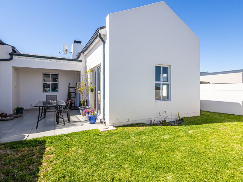 A well-maintained rear exterior view featuring a paved patio area, a neat lawn, and clean white building facades under a clear blue sky.