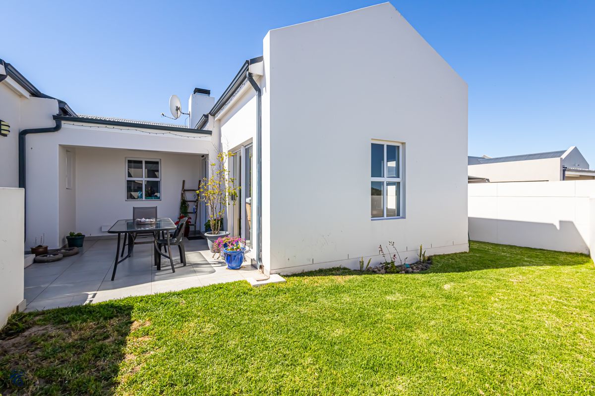 A well-maintained rear exterior view featuring a paved patio area, a neat lawn, and clean white building facades under a clear blue sky.