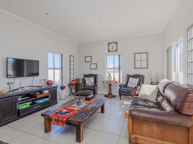 A bright and spacious living room featuring neutral tiled flooring, recessed downlighting, and large windows that provide ample natural light.