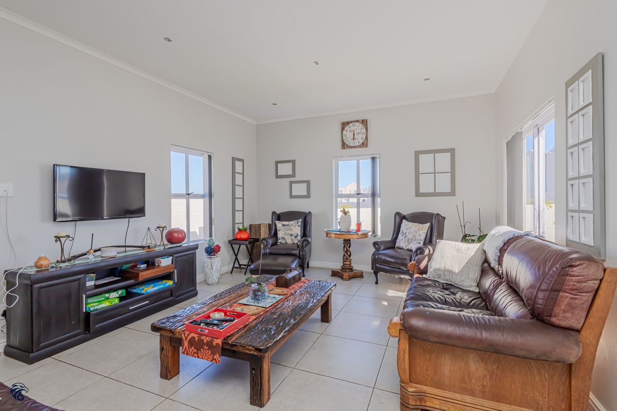 A bright and spacious living room featuring neutral tiled flooring, recessed downlighting, and large windows that provide ample natural light.