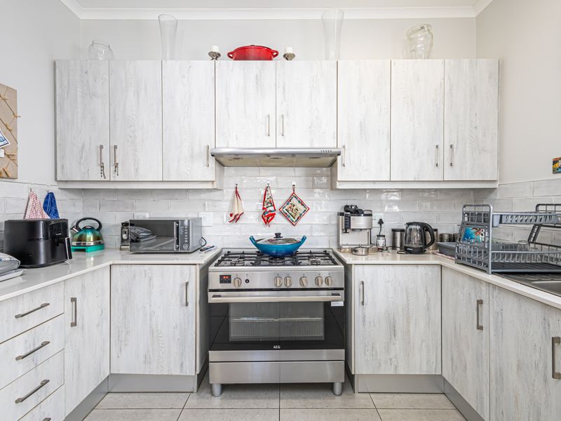 A functional kitchen featuring light wood-grain cabinetry, a stainless steel gas stove with extractor fan, subway tile backsplash, and tiled flooring.