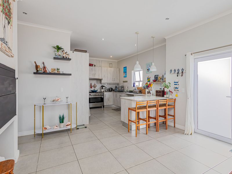 An open-plan kitchen featuring light-toned cabinetry, a breakfast island, tiled flooring, and direct access to the outdoors through a glass door.