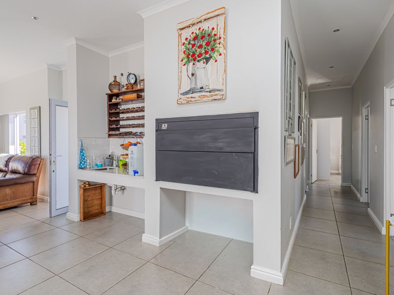 Open plan living area featuring a built-in fireplace, tiled flooring, and a convenient scullery nook with sink, leading into a hallway.
