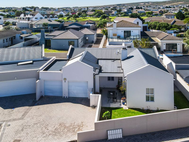 Aerial view of a modern residential property featuring a double garage, paved driveway, and a covered patio area within a suburban estate.