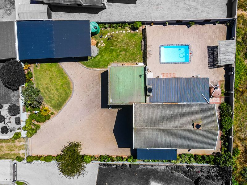 Aerial view of the property featuring a swimming pool, paved driveway, carport, and established garden areas within a fenced perimeter.