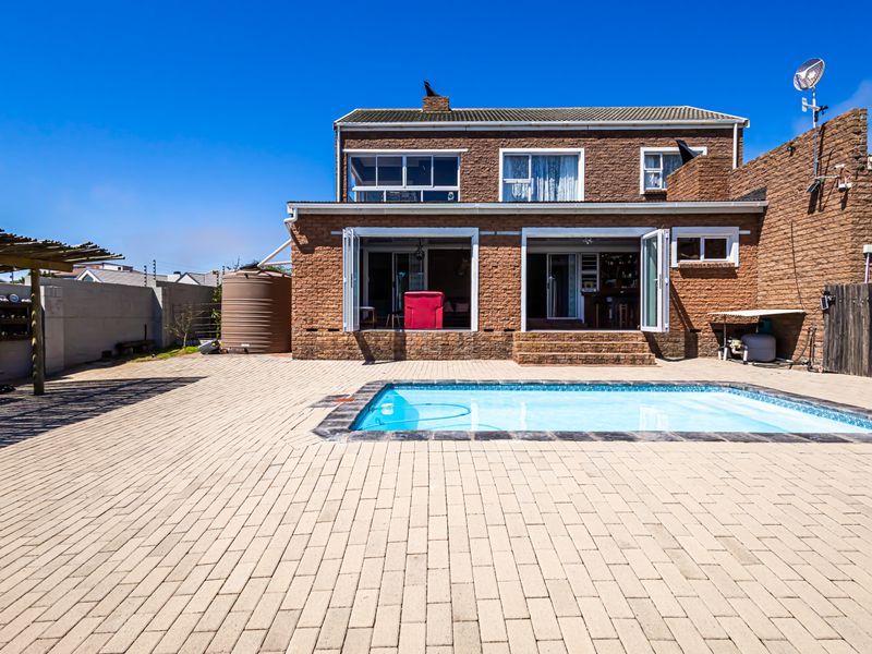 Rear exterior view of a brick house featuring a swimming pool, paved patio area, and a pergola, offering a functional outdoor entertainment space.