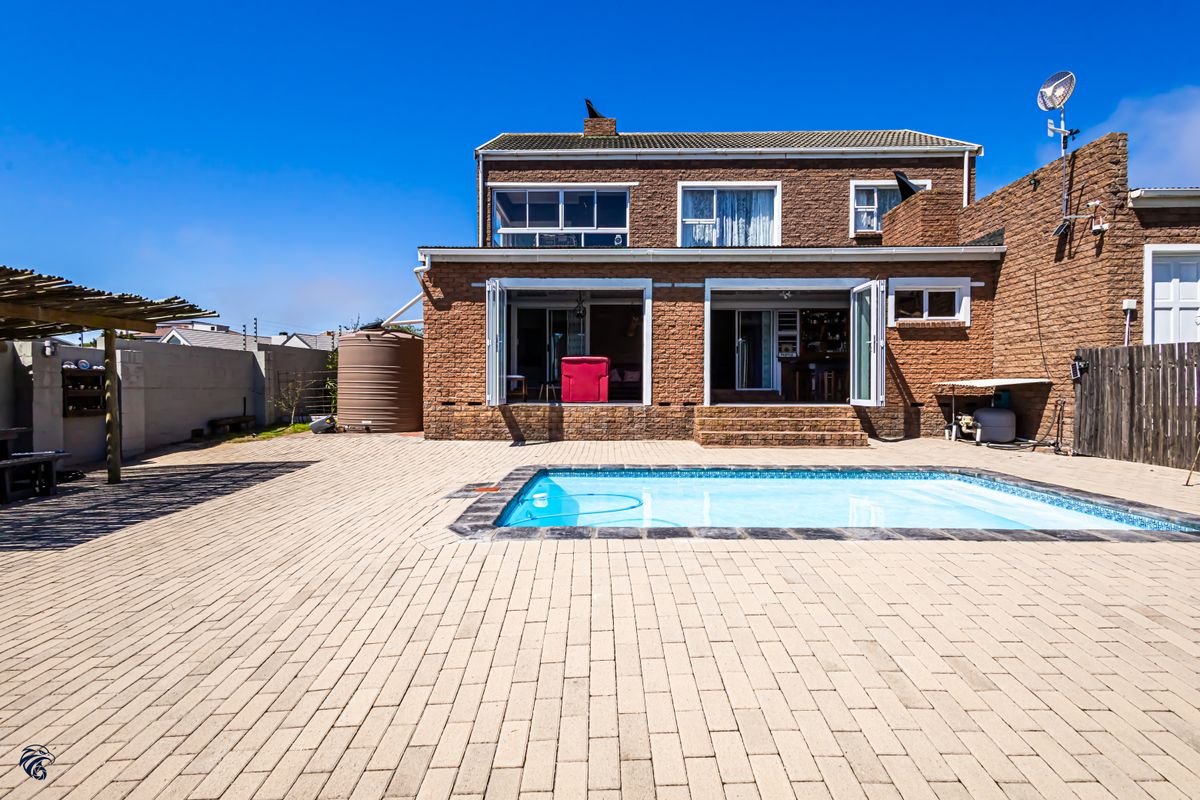 Rear exterior view of a brick house featuring a swimming pool, paved patio area, and a pergola, offering a functional outdoor entertainment space.