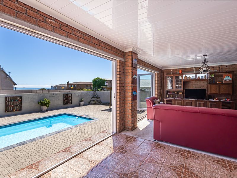 Covered patio area featuring tiled flooring, brick pillars, and direct access to an outdoor swimming pool and paved courtyard.