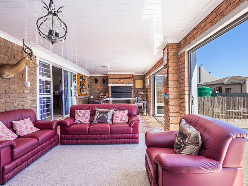 Spacious covered patio featuring exposed brick walls, a built-in braai, and large sliding doors opening directly onto the pool area.