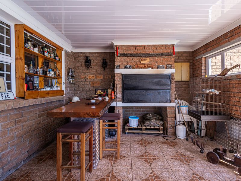 Covered patio area featuring a built-in braai, brick wall finishes, tiled flooring, and a custom built-in bar counter, ideal for outdoor entertaining.