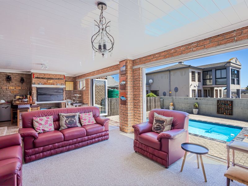 Spacious covered patio featuring exposed brick walls, a built-in braai, and large sliding doors opening directly onto the pool area.