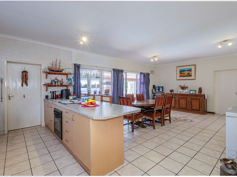 Spacious open-plan kitchen and dining area featuring tiled flooring, a central kitchen island with built-in oven, and sliding glass doors leading to the exterior.