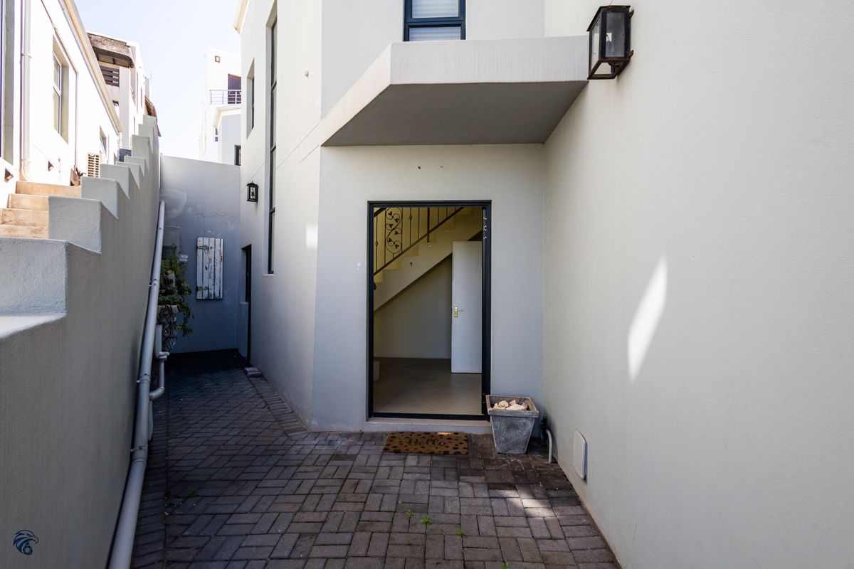 A paved rear exterior area featuring a staircase and access to the interior, with clean rendered walls and functional outdoor lighting.