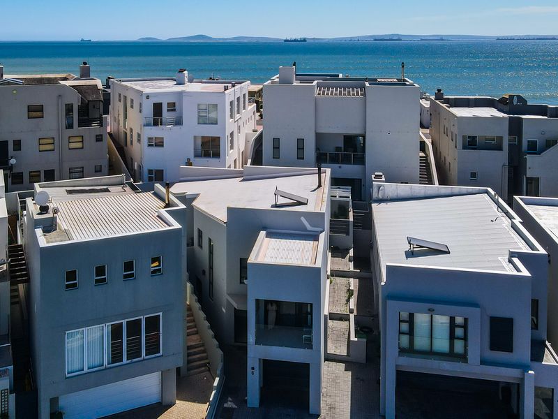 Aerial view of a modern coastal residential complex featuring contemporary architecture, flat roofs, solar water heaters, and paved access areas near the ocean.