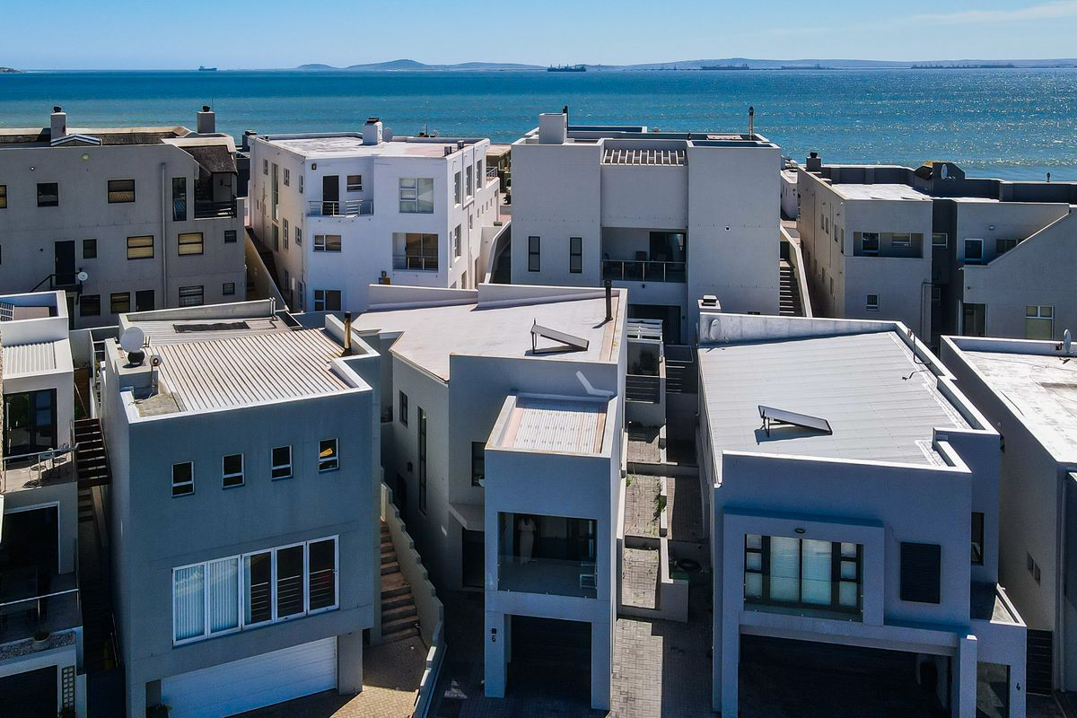 Aerial view of a modern coastal residential complex featuring contemporary architecture, flat roofs, solar water heaters, and paved access areas near the ocean.