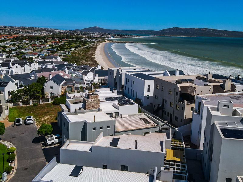 An aerial view of a coastal residential estate featuring modern homes with solar panels, situated directly along the beach.