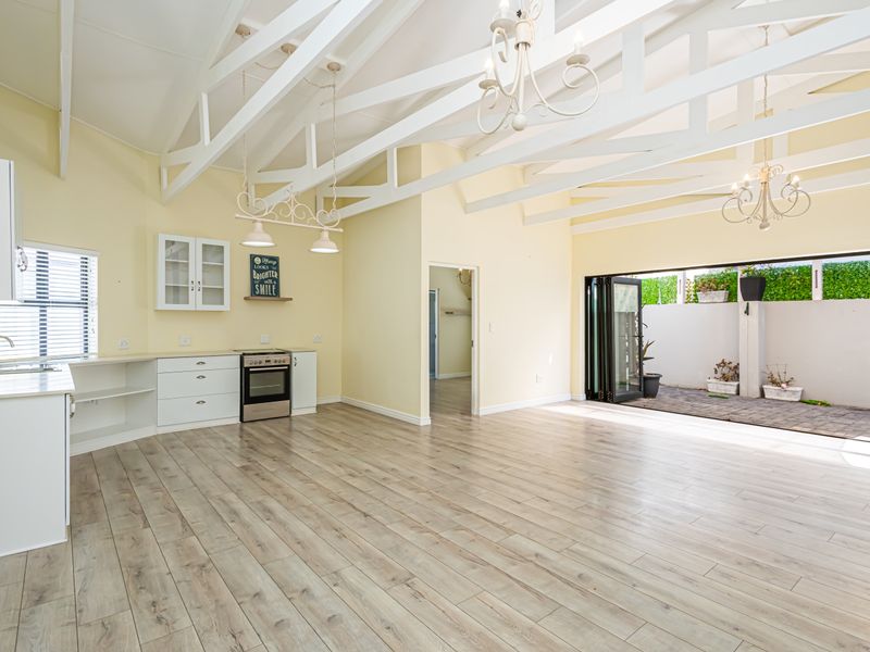 Spacious open-plan living area featuring exposed white timber trusses, laminate flooring, and a functional kitchen, opening directly onto a private paved patio.