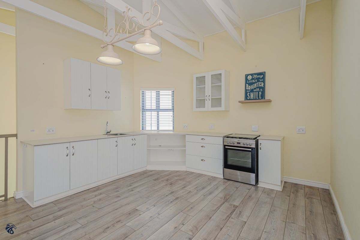 A bright, open-plan kitchen featuring white cabinetry, stainless steel oven and hob, laminate flooring, and exposed ceiling beams.
