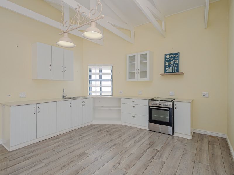 A bright, open-plan kitchen featuring white cabinetry, stainless steel oven and hob, laminate flooring, and exposed ceiling beams.