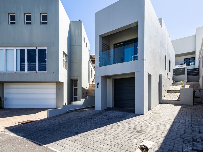 Modern multi-level residential facade featuring paved driveway access, integrated garages, and a private balcony with glass balustrade.
