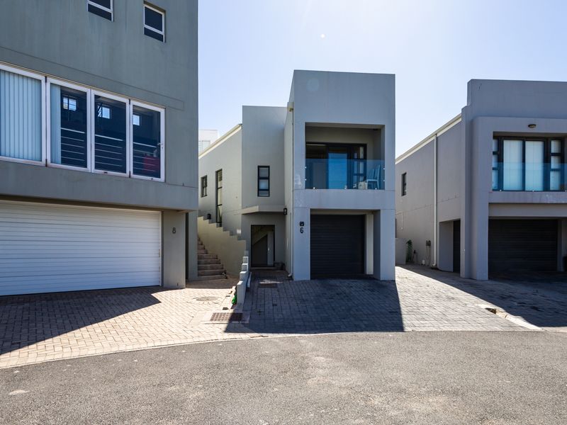 Front elevation of a modern multi-story residential property featuring paved driveways, integrated garages, and an upper-level balcony with glass balustrades.
