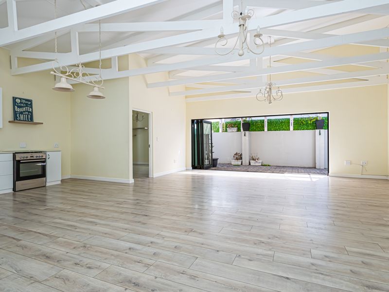 Spacious open-plan living area featuring exposed white timber trusses, modern laminate flooring, and seamless flow to an outdoor patio through large bi-fold doors.