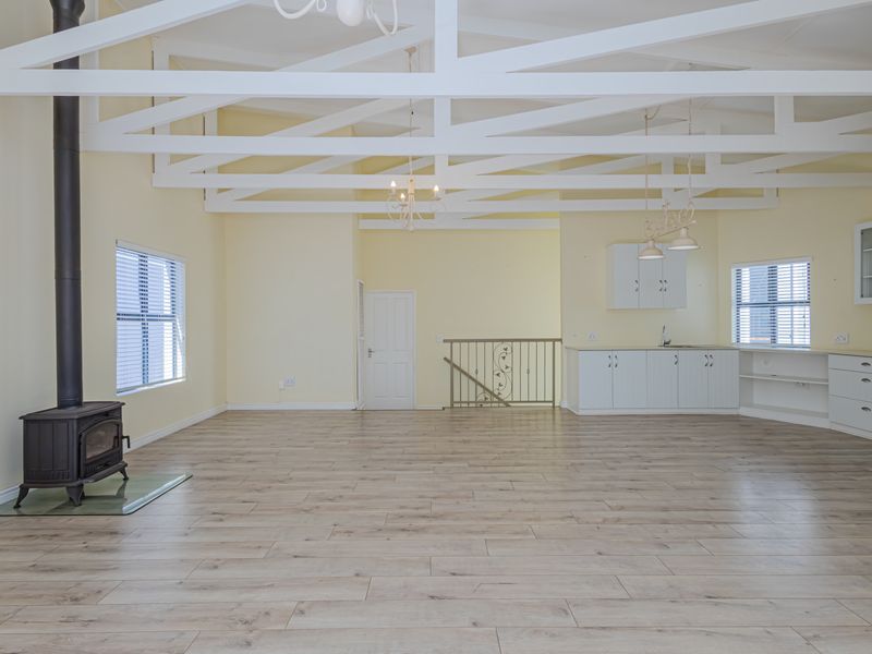 Spacious open-plan living area featuring high vaulted ceilings with exposed white trusses, a wood-burning stove, and a functional kitchen with modern cabinetry.