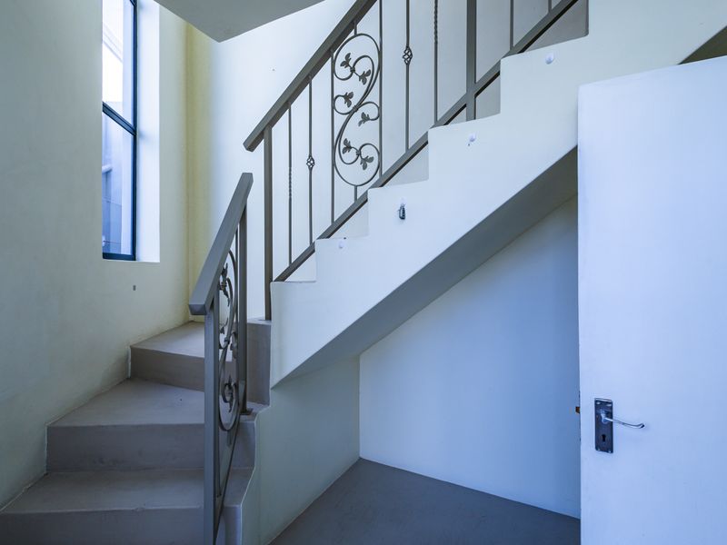 A bright, empty hallway featuring a staircase with decorative wrought iron railings and a clean, neutral interior finish.