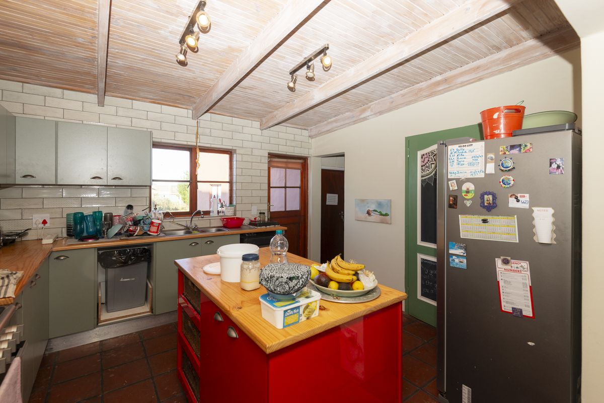 A rustic kitchen featuring a timber-clad ceiling, subway tile backsplash, terracotta flooring, and a central island, offering a functional layout with potential for modernization.