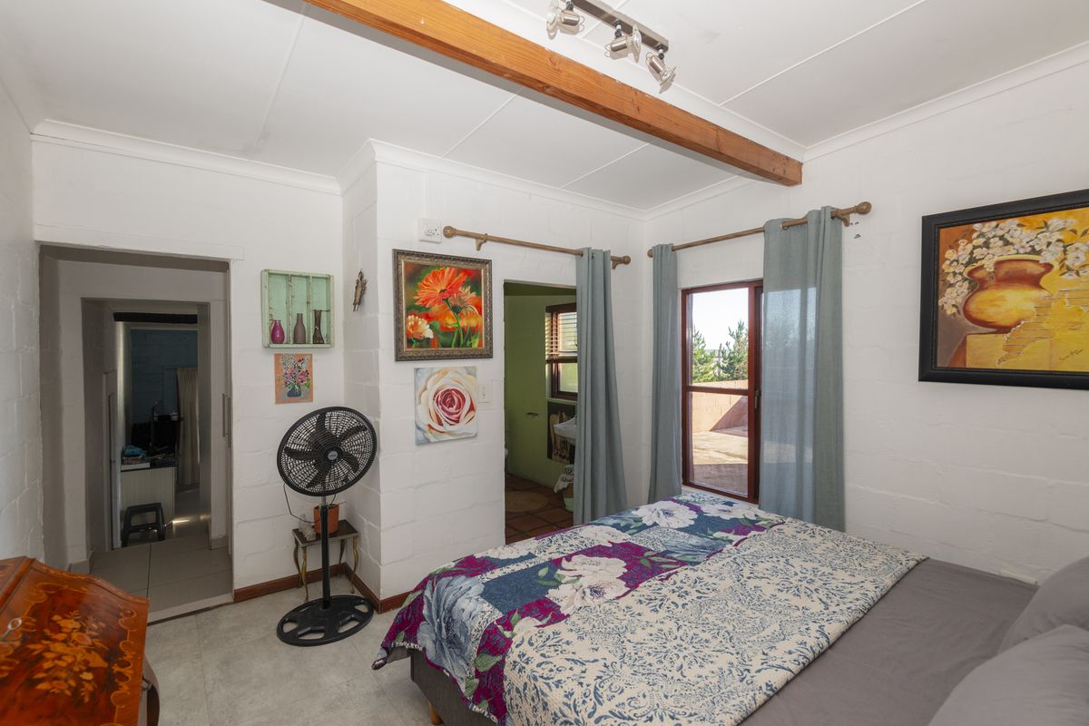 A bedroom featuring painted blockwork walls, an exposed timber ceiling beam, tiled flooring, and direct access to an outdoor area through a sliding glass door.